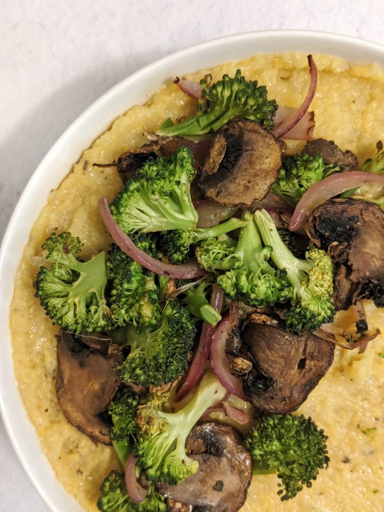 A bowl of creamy cheesy vegan polenta  topped with roasted broccoli and mushrooms is a thing you can do with store bought packaged polenta!